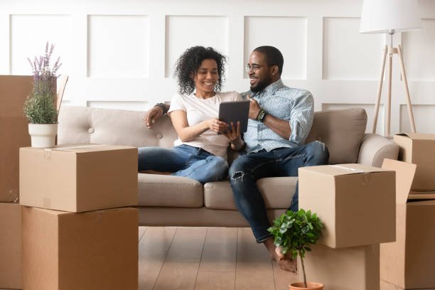 Happy couple using a tablet to plan their home move surrounded by packed boxes in Dubai.