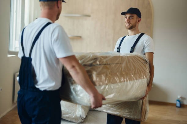 Two movers in uniforms carefully moving a wrapped sofa during a residential relocation in Dubai.