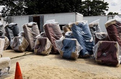 Plastic-wrapped furniture lined up outside moving truck for protection against Dubai heat and dust.